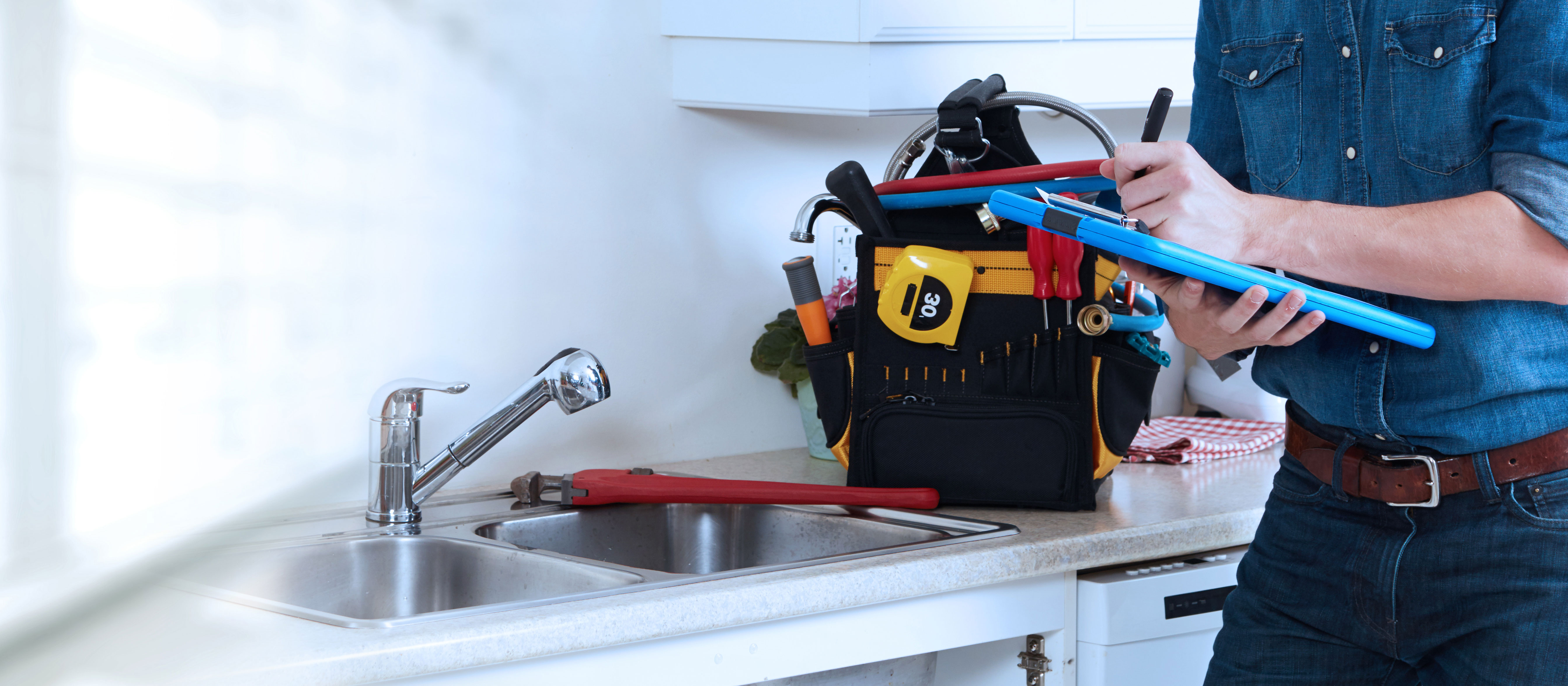 Plumber signing paperwork on tablet, standing in front of sink with toolbox