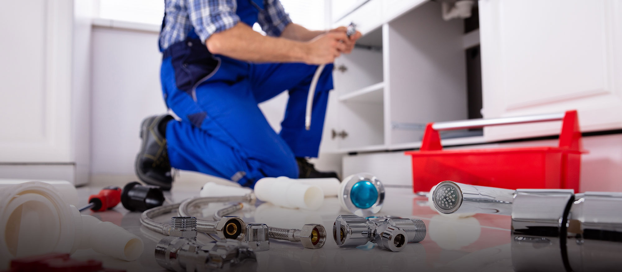 Plumber under sink with plumbing parts in the foreground